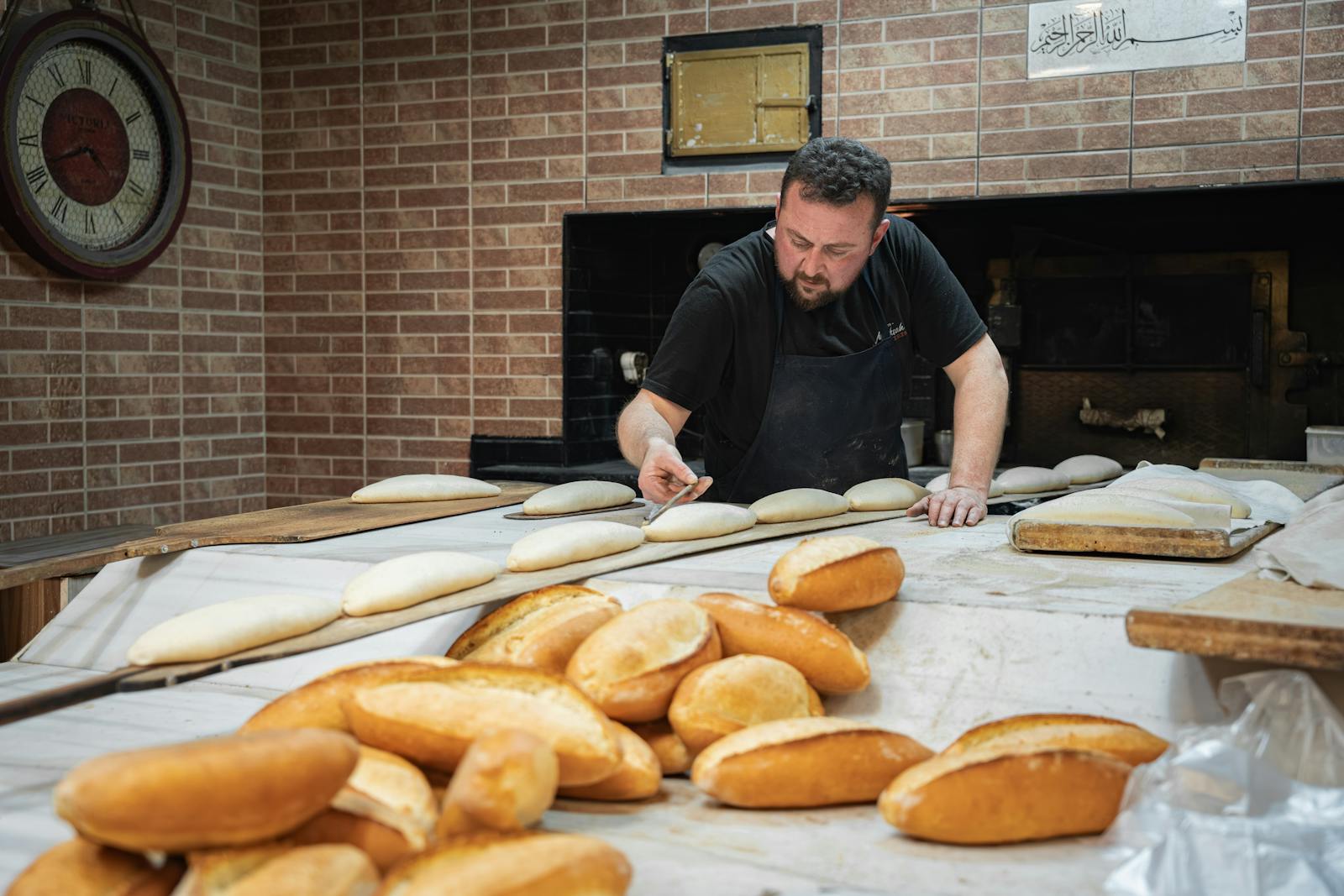 Bäcker formt Teig mit den Händen, im Hintergrund frisch gebackenes Brot.