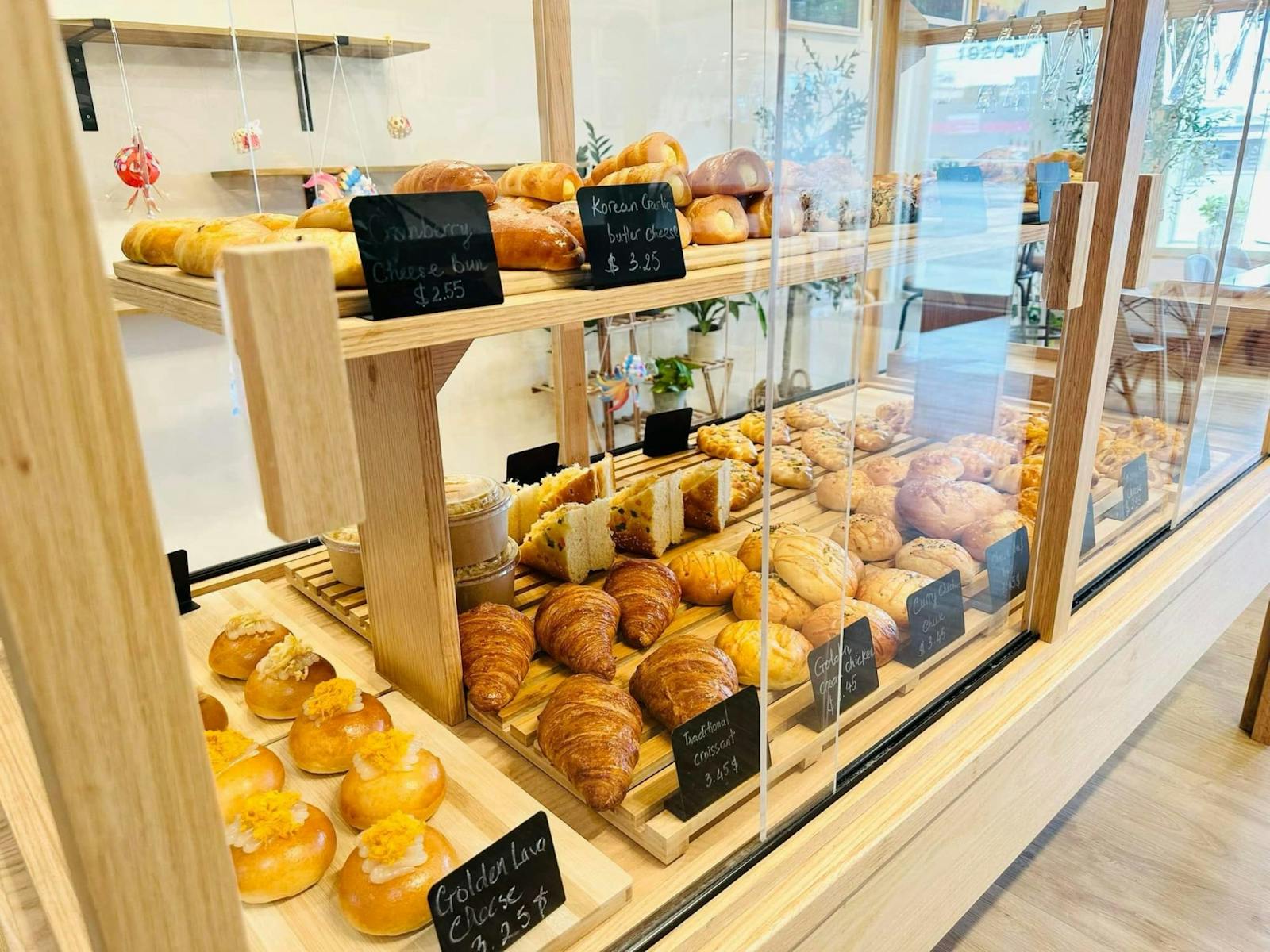 Helle Bäckerei-Vitrine mit frischen Backwaren, Croissants und Brötchen, mit Preisschildern und Tageslicht von außen.