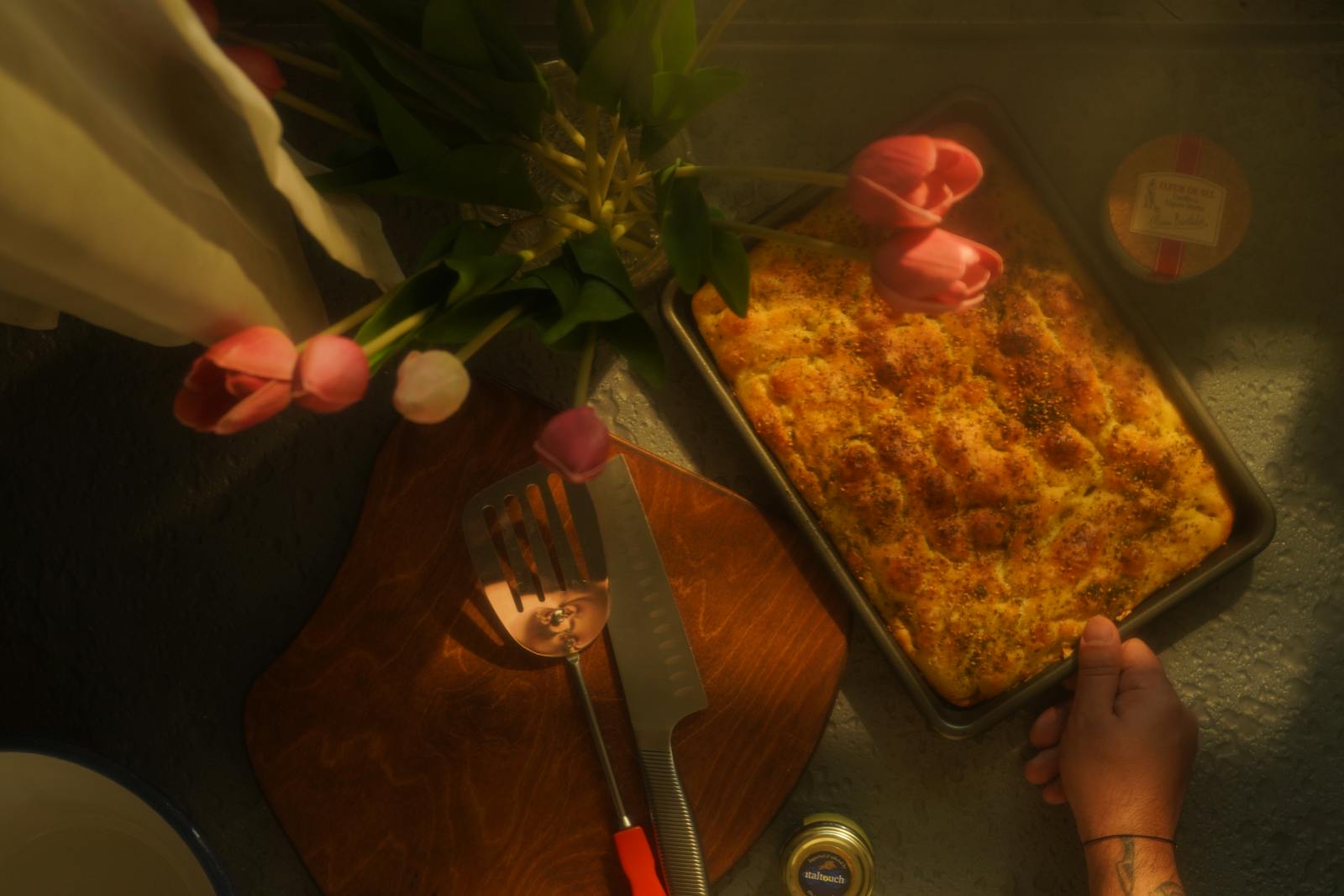Frische Focaccia in einem Blech, daneben Tulpen, weiches Streiflicht aus Fenster auf der rechten Seite.