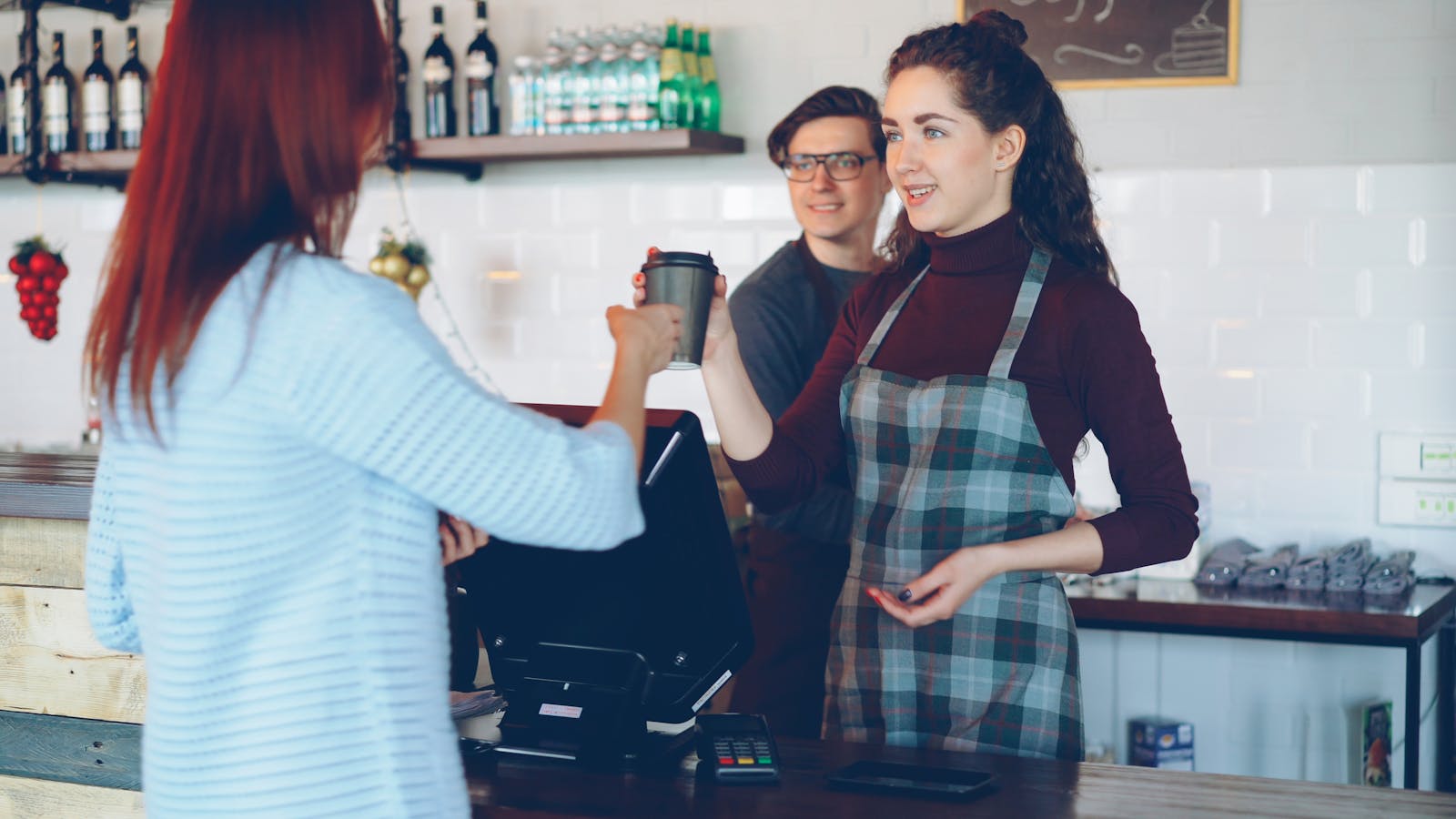 Barista reicht Kaffeebecher an Kundin in einem hellen Café.