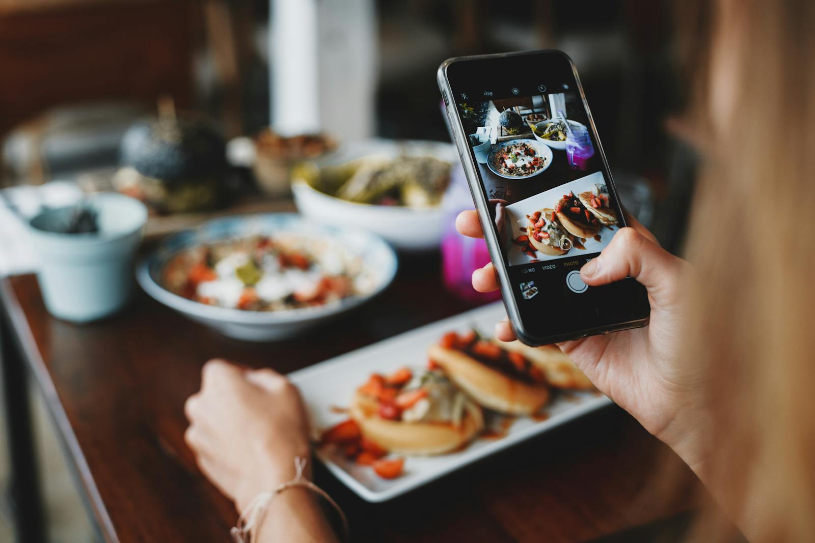 Hände halten ein Smartphone und fotografieren ein Gericht in einem warm beleuchteten Restaurant.