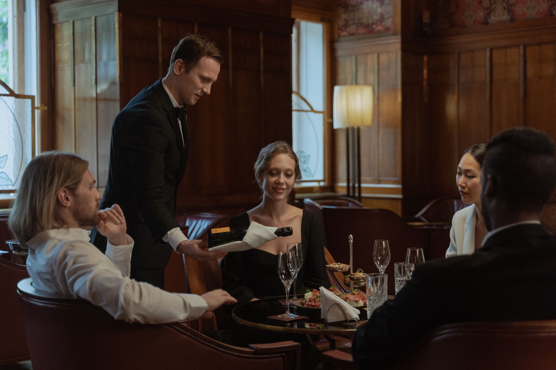 Servicekraft schenkt Gästen an einem gedeckten Tisch Wein nach.